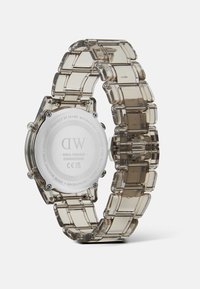 Reloj de plástico transparente con correa transparente, fondo de caja redonda de acero inoxidable plateado y logo grabado. Presenta un diseño de correa flexible.