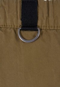 Brunt tyg med texturerad yta, utrustad med en svart rem och en silverfärgad metallring för fäste. Materialet verkar hållbart och lätt.