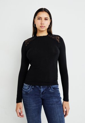 Haut noir à manches longues avec des détails en dentelle sur les épaules, design ajusté, texture douce, encolure arrondie, associé à un jean en denim bleu.