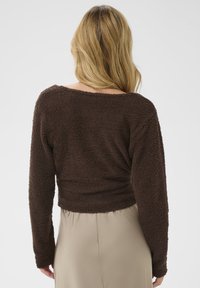 Barna, érdes, hosszú ujjú blúz, laza szabással és széles nyakkivágással, semleges, sima, lágy szoknyával párosítva. Hátsó nézet.