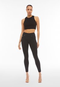 Musta, ribbineulottu crop top yhdistettynä mustiin korkeavyötäröisiin leggingseihin, joissa on taskut ja hopeanhohtoiset yksityiskohdat. Sileä, joustava materiaali.