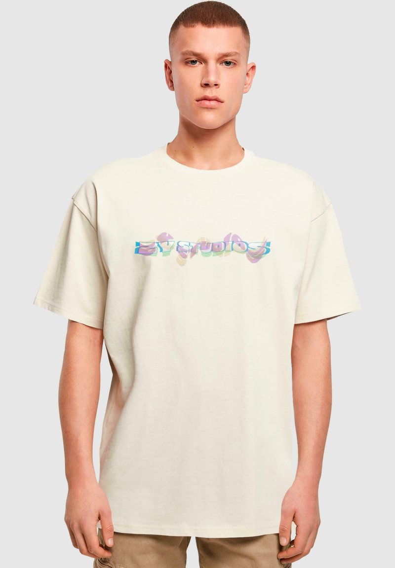 Beige oversize t-krekls ar krāsainu, rakstainu grafiku, kas attēlo tekstu "ZY STUDIOS". Izgatavots no mīkstas kokvilnas, ar brīvu piegriezumu un īsām piedurknēm.