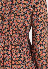 Tissu à motif floral dense marron, rose, bleu et blanc sur fond noir, avec taille froncée et manches longues.
