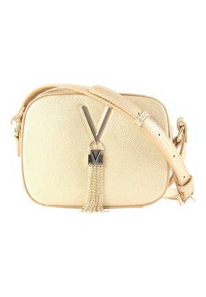Beige gestructureerde crossbodytas met verstelbare riem, metalen "V"-embleem en gouden kettingkwast detail aan de voorkant.