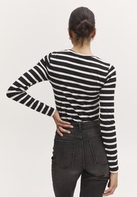Schwarz-weiß gestreiftes Langarmoberteil mit Rundhalsausschnitt, kombiniert mit hochgeschnittenen dunkelgrauen Jeans, die Taschen auf der Rückseite haben.