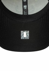 Gros plan sur l'intérieur de la visière d'une casquette noire montrant un petit autocollant d'authenticité avec un graphique de basket-ball et un numéro de série.