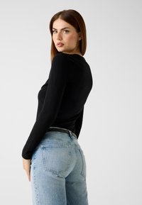 Schwarzes Langarmshirt mit figurbetontem Schnitt, kombiniert mit hellblauen, hoch taillierten Jeans mit fünf Taschen und einem schwarzen Gürtel.