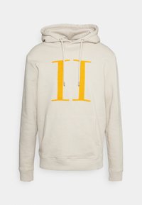 Sudadera con capucha beige que presenta un gran gráfico amarillo "II", cuello con cordón y bolsillo frontal tipo canguro. Textura suave con puños acanalados.
