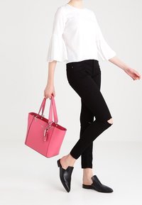 Różowa torba na ramię o gładkim materiale, prostokątnym kształcie, z dwoma uchwytami i srebrnym okuciem, zestawiona z czarnymi podartymi dżinsami i czarnymi butami wsuwanymi.