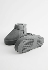 Graue Wildleder-Stiefeletten mit Kunstfellfutter, ausgestattet mit einer flachen Gummisohle und einem strukturierten Profilmuster an der Unterseite.