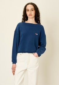 Felpa blu corta con maniche lunghe, caratterizzata da un piccolo design multicolore ricamato sul petto e un dettaglio di orlo grezzo.
