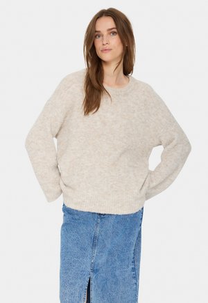 Helle beige, strukturierte Strickjacke mit lockerem Schnitt, rundem Ausschnitt und abgesenkten Schultern, kombiniert mit einem den mid-length Jeansrock.