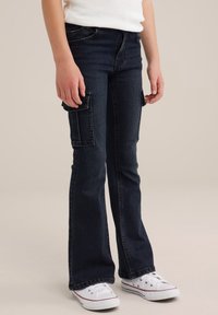 Mörkblå utsvängda cargojins med framfickor och sidofickor, tillverkade av denim, i kombination med vita sneakers.