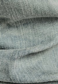 Ljust blå denimtyg med en strukturerad väv, med mjuka veck och subtil skuggning, som visar materialets mjukhet och flexibilitet.