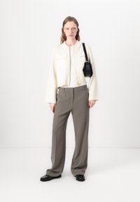 Κομμένο λευκό μπουφάν με δύο μπροστινές τσέπες, συνδυασμένο με γκρι παντελόνι φαρδιάς γραμμής. Μαύρ�η τσάντα ώμου και υφασμάτινα μαύρα παπούτσια ολοκληρώνουν την εμφάνιση.