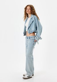 Chaqueta de mezclilla recortada de color azul claro con botones dobles, combinada con jeans rectos azul claro. También incluye una camiseta blanca y zapatillas.