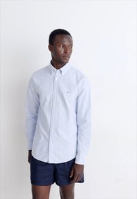 Lichtblauw overhemd met knopen van katoen, met een kraag en lange mouwen. Gepaard met marineblauwe shorts. Eenvoudig ontwerp, geen patronen.