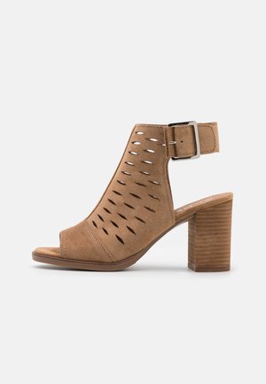 Braune Wildleder-Sandalette mit offenem Zehenbereich, perforiertem Design, verstellbarem Knöchelriemen und Blockabsatz aus Holz, Seitenansicht.