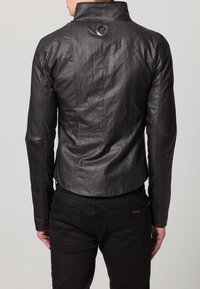 Czarna skórzana kurtka z wyraźnie zarysowanym kołnierzem, teksturowaną powierzchnią, skróconym fasonem i metalowym okrągłym detalem z tyłu.
