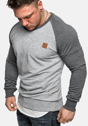Graues und hellgraues Sweatshirt mit abgerundetem Saum, gerippten Bündchen und einem kleinen braunen Lederetikett auf der Brust.