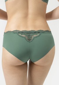 Groene slips met kantaccent, gemaakt van een zachte stof met een bloemenkantdetail aan de achterkant, wat een naadloos design en een gladde textuur benadrukt.