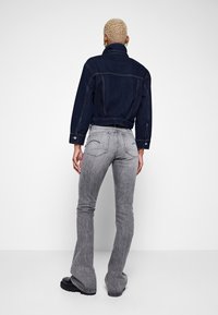 Chaqueta de mezclilla oscura con un diseño corto, combinada con jeans acampanados gris claro que presentan detalles sutiles de costura y un ajuste ceñido en las caderas.