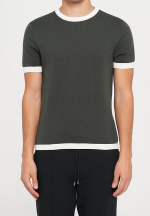 Dunkelgraues Strickshirt mit kurzen Ärmeln und weißem Besatz am Kragen, an den Ärmelbündchen und am Saum, getragen von einer stehenden Person.