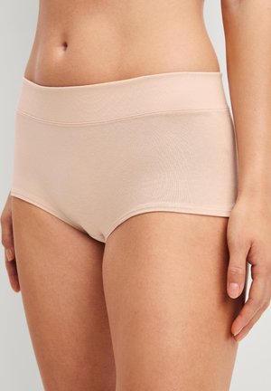 Frau trägt nahtlose, hautfarbene High-Waist-Slips, die Taille, Hüften und obere Oberschenkel vor neutralem Hintergrund zeigen.