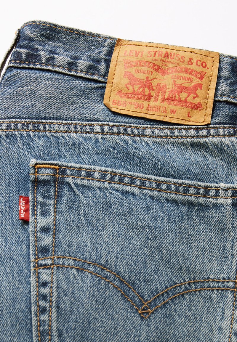 Primer plano de un bolsillo trasero de unos vaqueros azules con la etiqueta roja de Levi's y un parche de cuero marrón de la marca en la cinturilla.