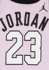 Lyserød trøje med sorte "JORDAN"-tryk og nummeret "23" i hvidt, omkranset af sort. Inkluderer en sort krave og Jumpman-logo.