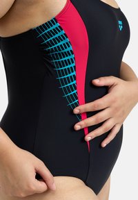 Maillot de bain noir avec un panneau latéral rose vif orné d'un motif à carreaux bleu. Le matériau est lisse et conçu pour épouser les formes.