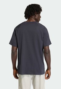 Tmavomodré tričko s krátkymi rukávmi, voľného strihu, s raglánovými rukávmi a hladkým povrchom, nosené s nohavicami svetlej farby.