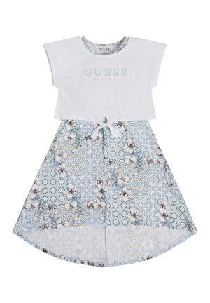 Hvid kortærmet cropped top med "Guess Los Angeles" tekst over en høj-lav blomster- og mønstret nederdel med bundet detalje foran.