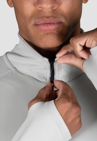 Hellgrau, Langarmshirt mit einem hohen Kragen und teilweise Reißverschluss vorne. Glatter, elastischer Stoff mit Daumenlöchern in den Ärmeln.