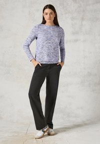 Pullover aus mehrfarbigem lilanem Strick, Rundhalsausschnitt und langen Ärmeln; kombiniert mit dunkelgrauen, weit geschnittenen Hosen und weißen Sneakers mit schwarzem Besatz.