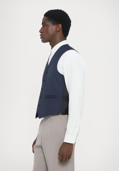 Marineblauer Weste mit glatter Textur, sechs Knöpfen und zwei Fronttaschen, kombiniert mit einem weiß gestreiften Hemd und hellen Hosen.