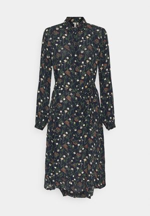 Kukkaprintillä varustettu mekko, jossa on pitkät hihat, kaulus ja solmittava vyötärö. Tumma tausta, jossa valkoisia ja värikkäitä kukkakuoseja, kevyt kangas.