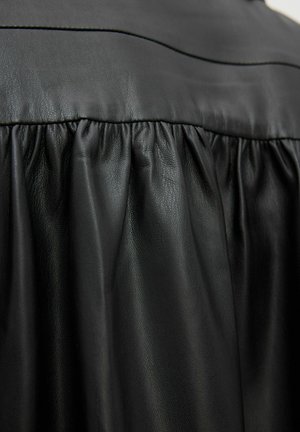 Abito in pelle nera con una vita arricciata, texture liscia e leggero lucido, caratterizzato da dettagli strutturati nel busto.