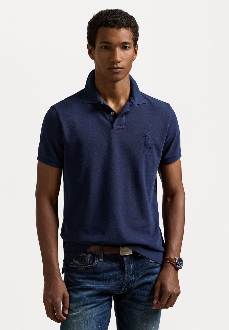 Polo navy de algodón, con un cuello clásico, mangas cortas y un discreto logo bordado en el pecho. Combinado con jeans azules.