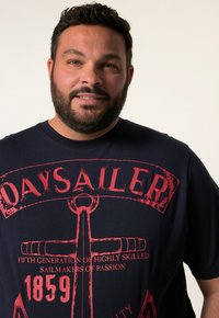 Námořnické tričko z bavlny s červeným grafickým designem, na kterém je ve středu slovo "DAYSAILER" a motiv kotvy.