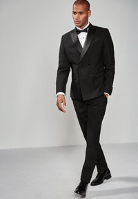 Schwarzer Smoking mit satinierter Spitzenklappe, weißem Hemd, schwarzem Fliegenbinder, maßgeschneiderten Anzughosen und polierten schwarzen Dressschuhen.