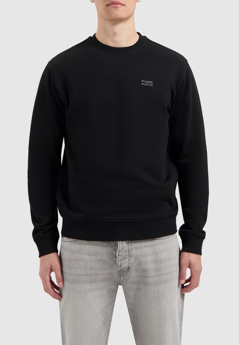 Zwarte sweatshirt van een katoenmix, met een ronde hals, ribgebreide boorden en onderzoom, en een klein gedrukt logo op de borst. Gepaard met lichtgrijze jeans.