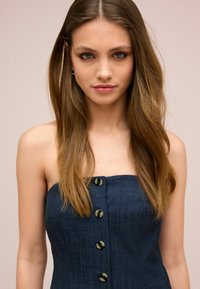 Strapless Jeanskleid in Dunkelblau, mit sechs vorderen Knöpfen in glänzender Ausführung. Glatte Textur, figurbetonte Form und keine sichtbaren Muster.