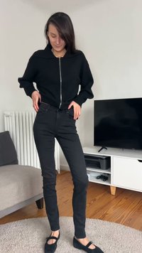 Črni pulover z zadrgo, črne prilegajoče se kavbojke in črne balerinke. Preprost dizajn, gladka tekstura in enotna barva po vsem outfitu.