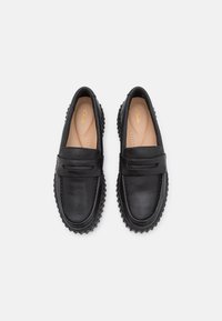 Mocassins noirs en cuir à finition lisse, avec un accent cousu et une semelle en caoutchouc à crampons saillants. Doublure intérieure confortable.