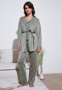 Olijfgroene pyjama-set met kanten details en een bijpassende riem. Zachte, fluweelachtige textuur; bevat een langemouwen jack en aansluitende broeken.
