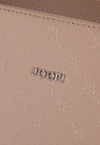 Bež usnjena denarnica z teksturiranim površjem, ki vključuje vtisnjen cvetlični vzorec in srebrni logotip "JOOP!", ki je jasno vidno.