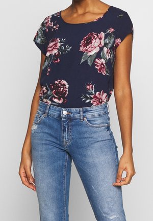Blomster navy top med korte ærmer, prydet med røde og pink rosenprints, parret med lyseblå slidte jeans og en sølvknapdetalje.