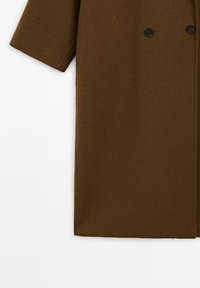 Brun ullblandad kappa med korta ärmar, dubbelknäppning, slät textur och svarta knappaccenter.