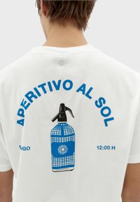 Weißes T-Shirt mit einem blauen Grafikmotiv eines Sprayflaschen. Der Text "APERITIVO AL SOL" steht in fetten blauen Buchstaben über und unter der Flasche.